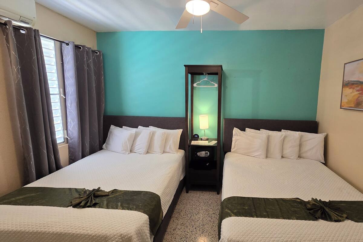 Una habitación de hotel con dos camas, una mesita de noche con lámpara, un espejo y un cuadro en la pared.