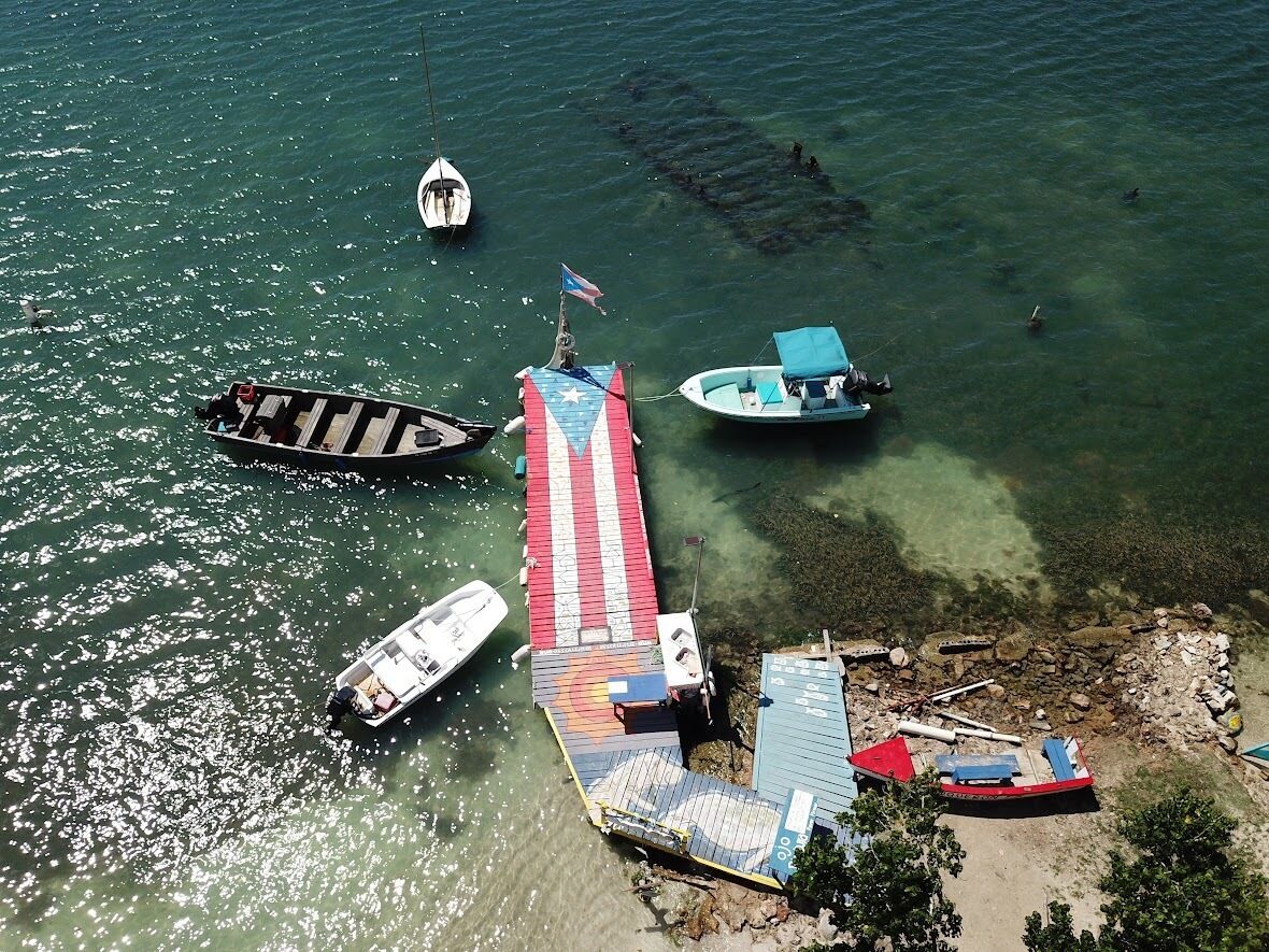 An aerial view of a dock with several boats, a flag, and a clear water body.