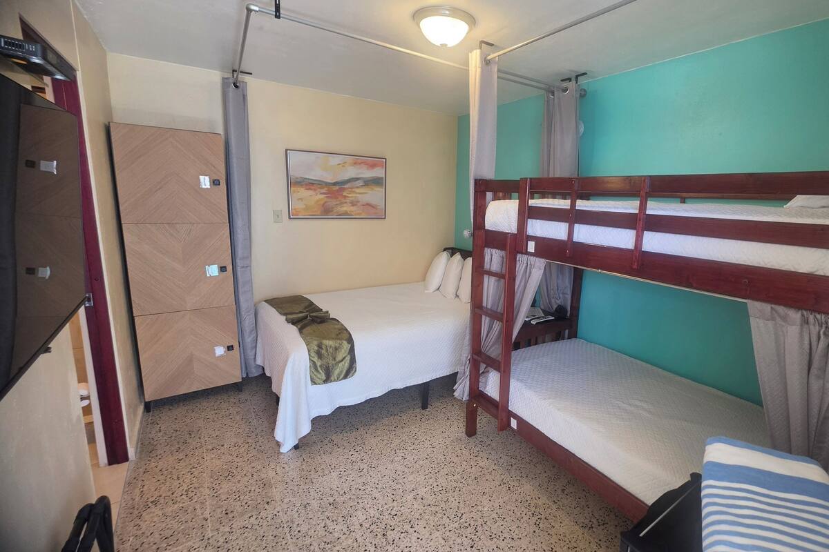 Una habitación con literas, una cama individual, un armario, un cuadro y una lámpara en el techo.