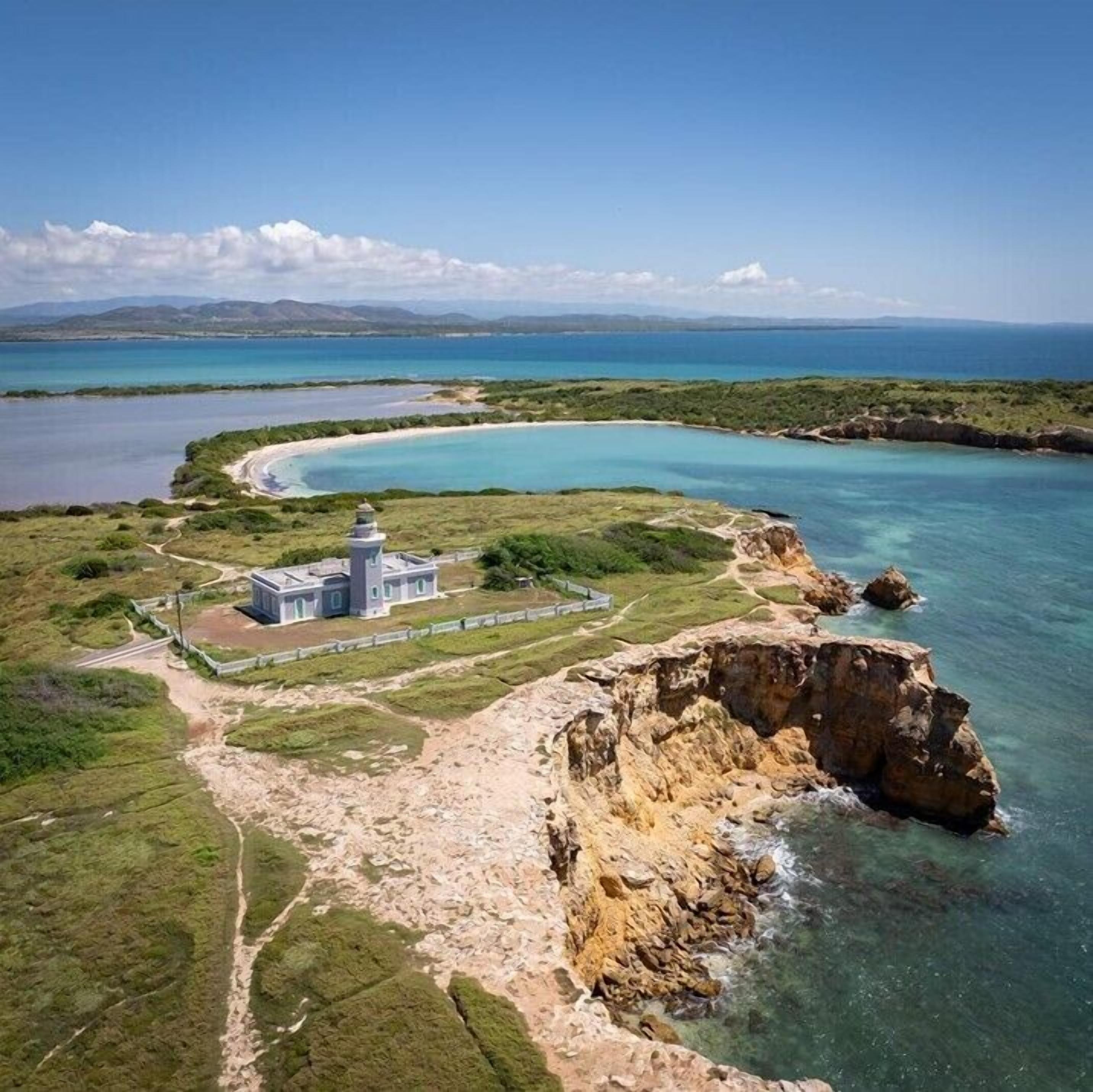 A coastal landscape with a lighthouse, clear blue waters, and a rocky shoreline.