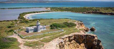 A coastal landscape with a lighthouse, clear blue waters, and a rocky shoreline.