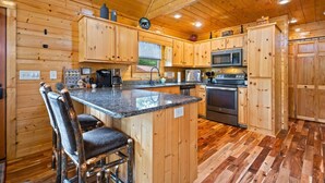 A wooden cabin kitchen with a granite countertop, stainless steel appliances, and a bar stool. - Stunning  chalet close to Murphy. Hot Tub, Fire Pit, Dog Friendly, Ample Parking (Murphy)