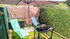 Un espace patio aménagé avec un barbecue, une table et une chaise placés sous un parasol.