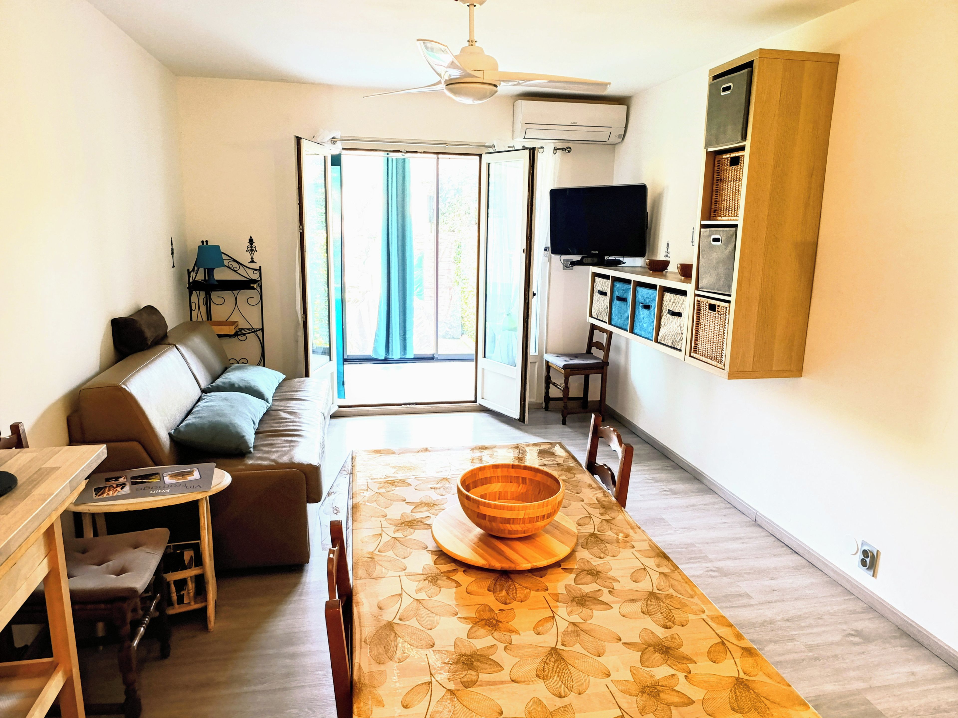 Un salon avec un canapé, une table à manger avec un saladier, un téléviseur et un ventilateur de plafond.