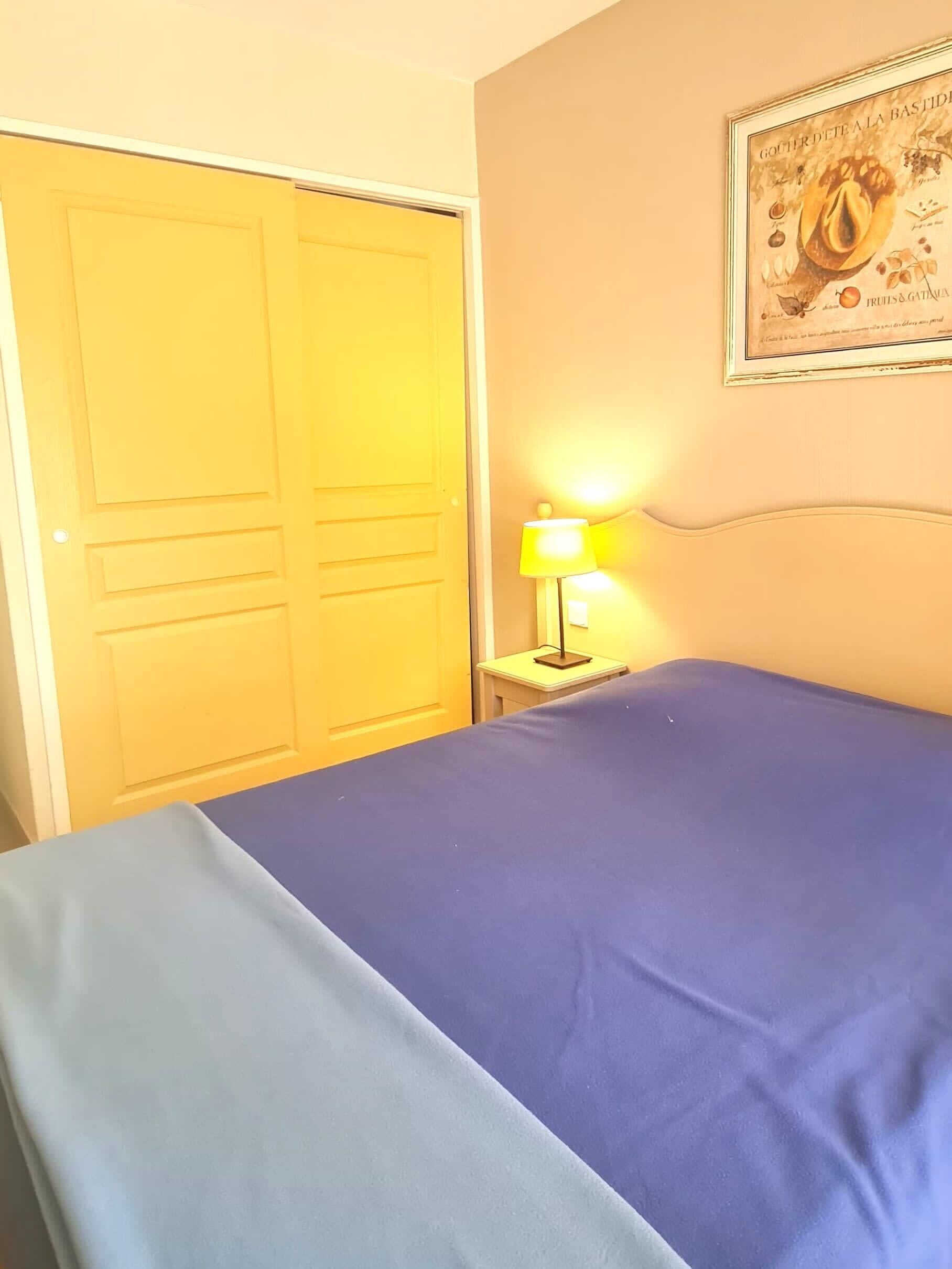 A room with a bed, a nightstand with a lamp, and a door.