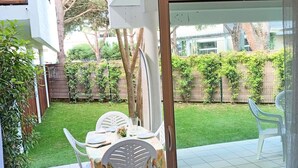 A patio area with a table set for two, surrounded by white chairs, and a view of a well-maintained garden with a wooden fence and greenery.