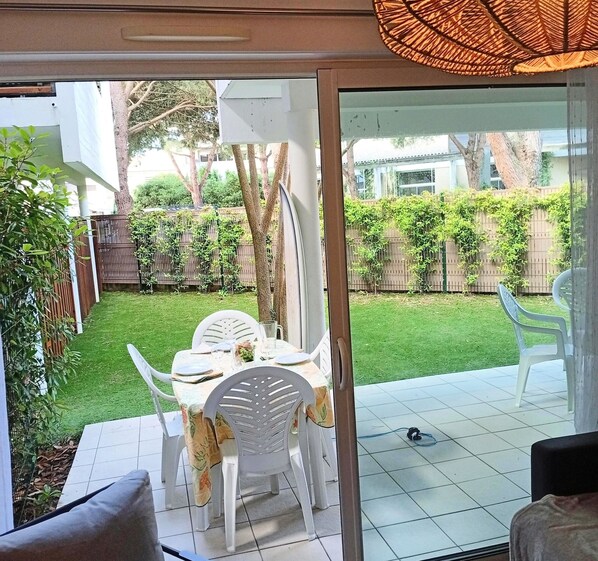 A patio area with a table set for two, surrounded by white chairs, and a view of a well-maintained garden with a wooden fence and greenery.