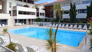 A modern hotel with a swimming pool, white lounge chairs, and a tiled deck.