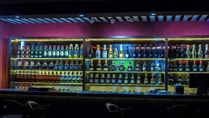 Un bar con varias estanterías llenas de botellas de licor, taburetes y un techo con iluminación empotrada.