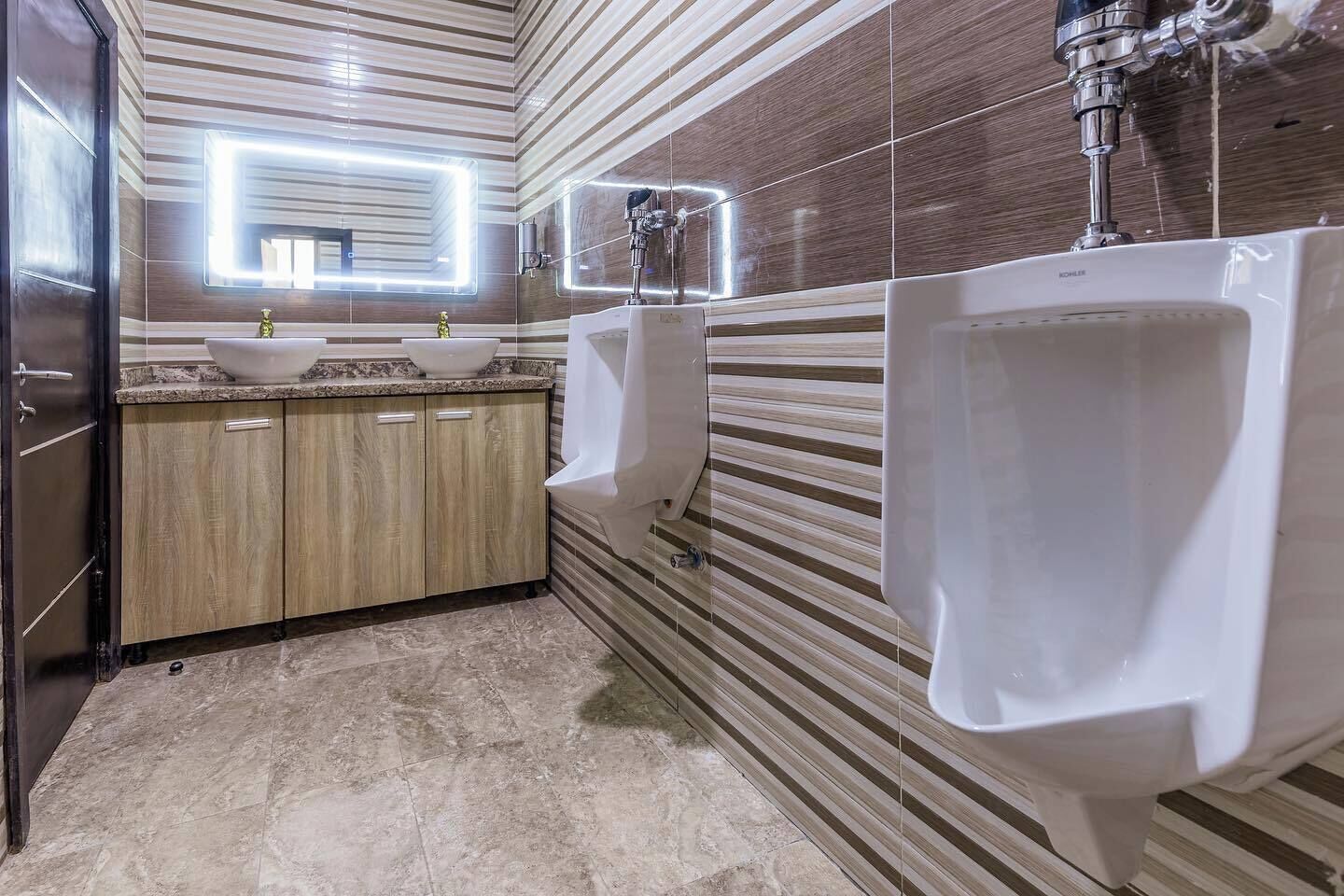 A modern bathroom with two sinks, a vanity, and urinals.