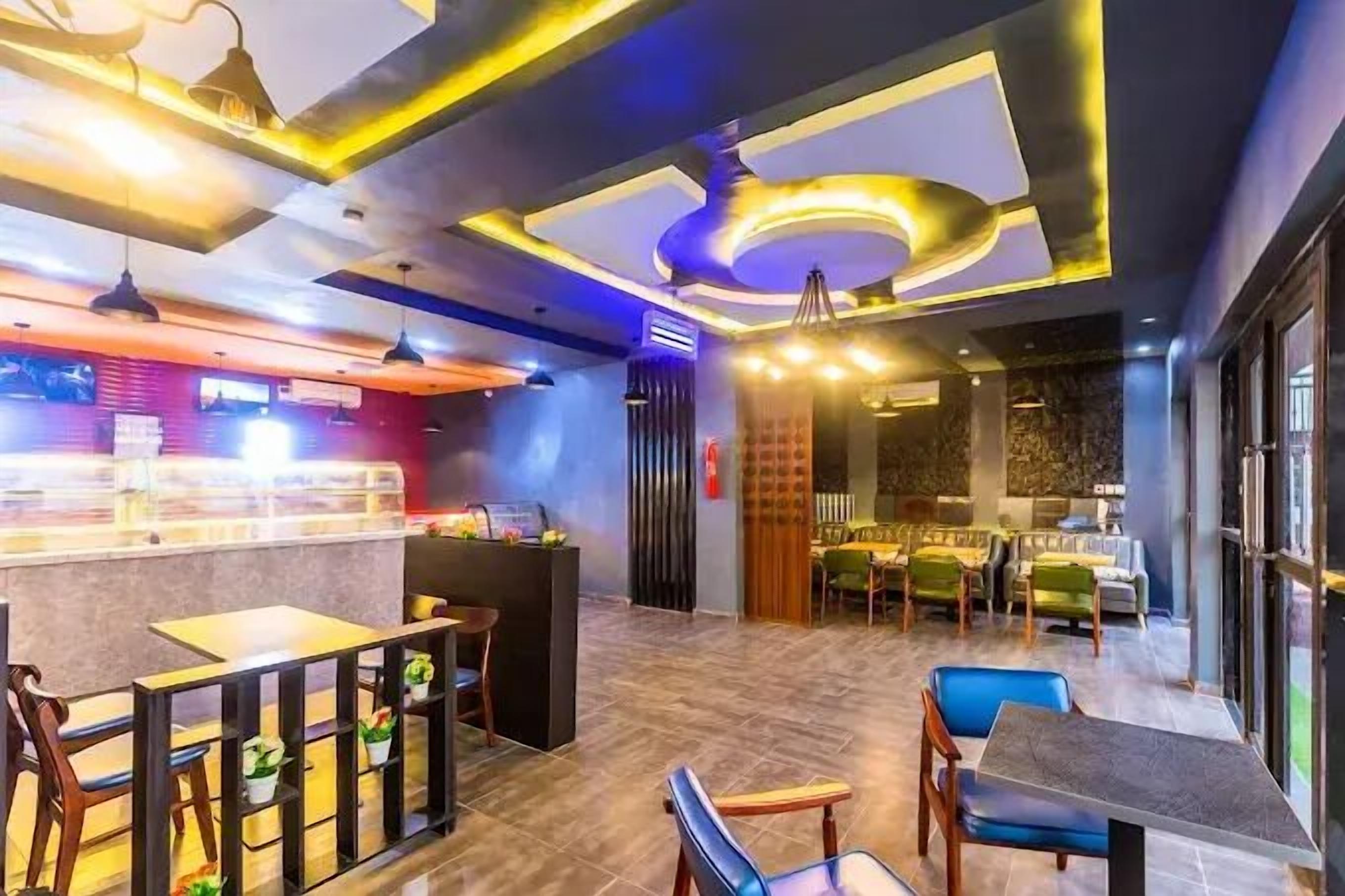 Un interior de restaurante moderno con zona de bar, disposición de mesas y iluminación decorativa en el techo.