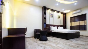Habitación de hotel moderna con una cama grande, un escritorio, una silla y una mesita pequeña. Hay estantes en la pared y un equipo de aire acondicionado.