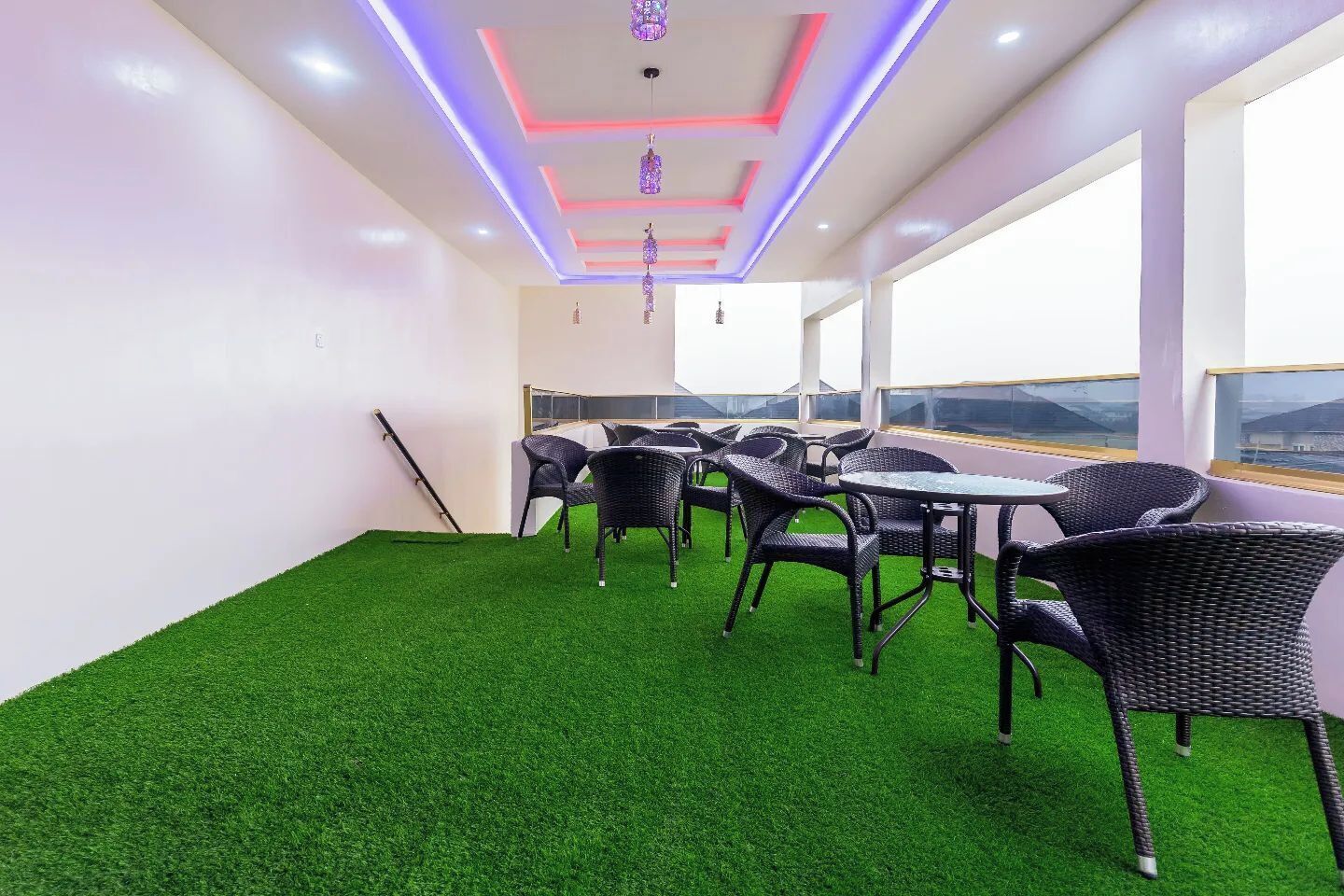 A room with artificial green turf, wicker furniture, and a view through large windows.