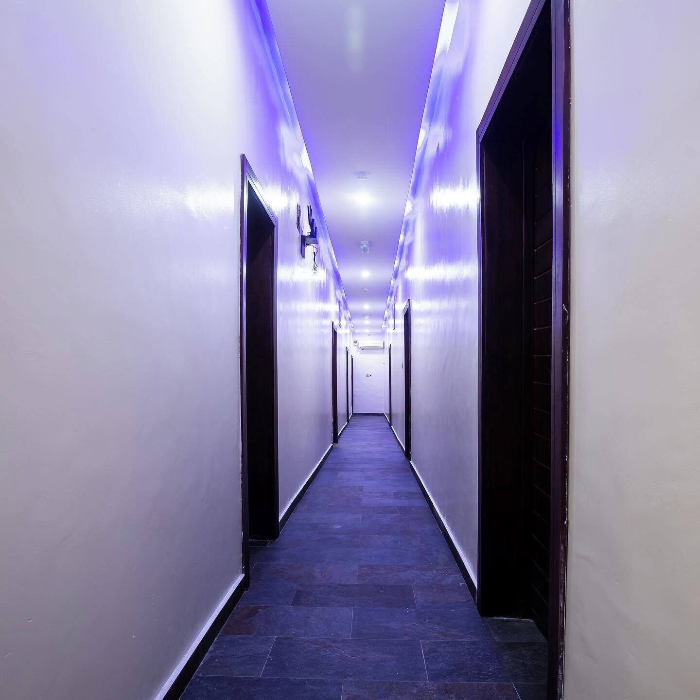 A long, narrow hallway with a dark floor and white walls, illuminated by blue lighting.