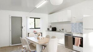 Een moderne keuken met witte kasten, een eettafel met stoelen, een fornuis en een magnetron.