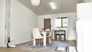 Een eethoek met een tafel en stoelen, een bijzettafeltje met een vaas, een raam met uitzicht en een deur met muggengaas.