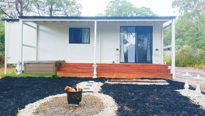 Een klein, gelijkvloers huis met een veranda, een zwarte deur en een klein raam.
