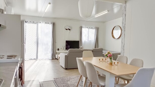 Een moderne woonkamer met een bank, televisie en een eetgedeelte met stoelen en een tafel.