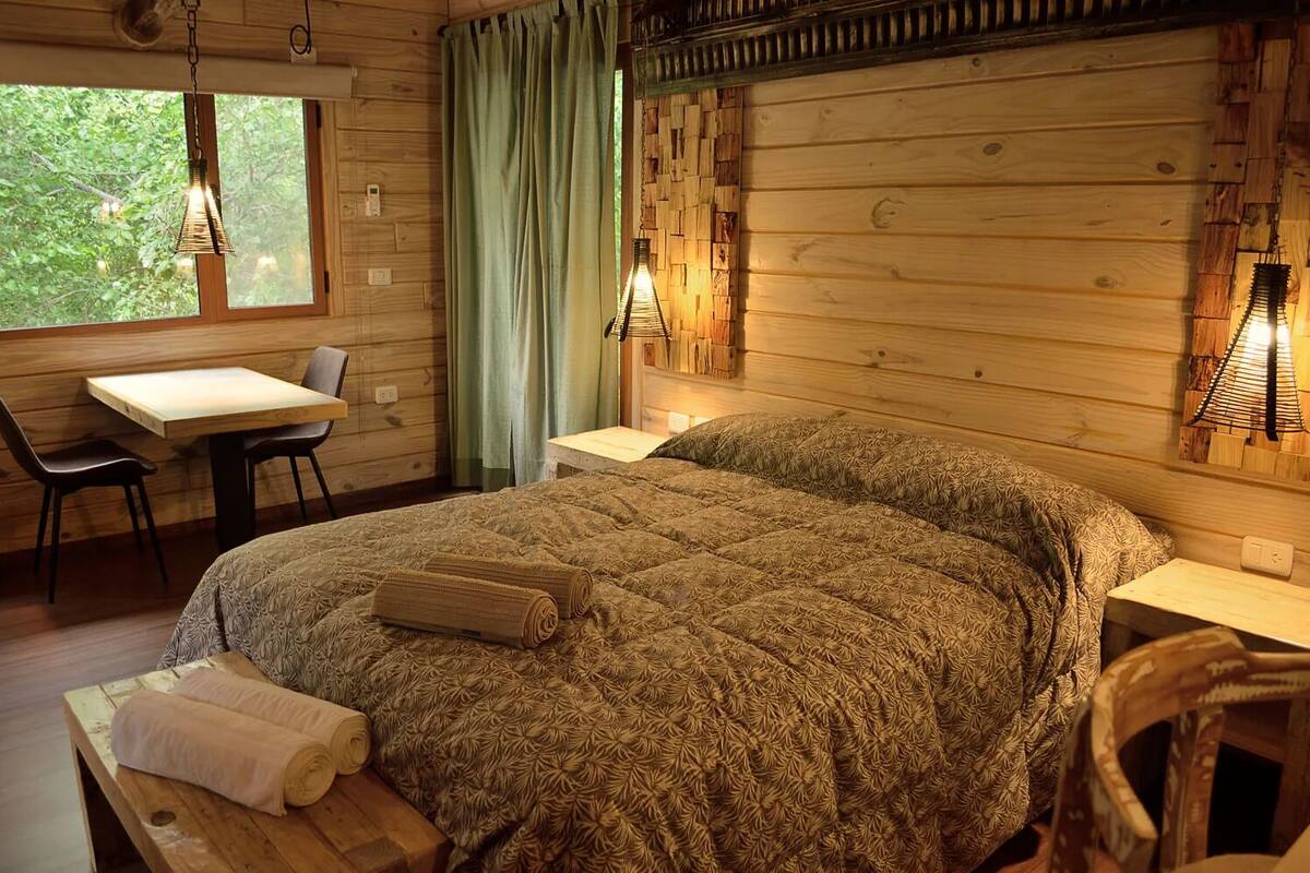 A cozy wooden room with a large bed, a small table, and chairs.