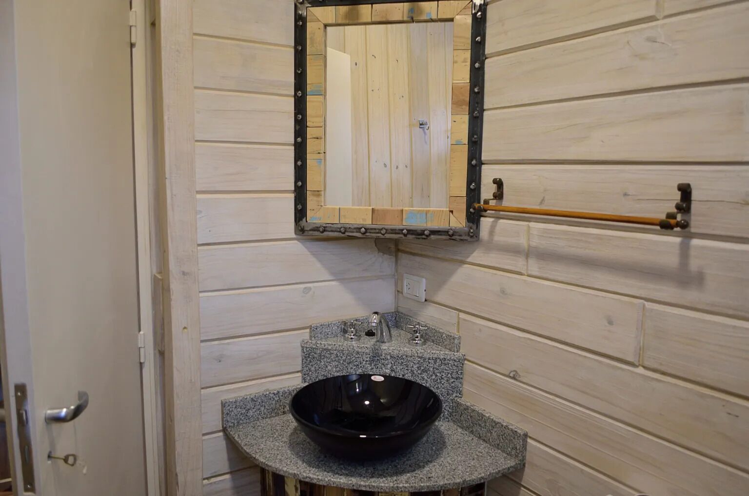 A bathroom with a wooden wall, a sink with a black basin, and a mirror with a metal frame.