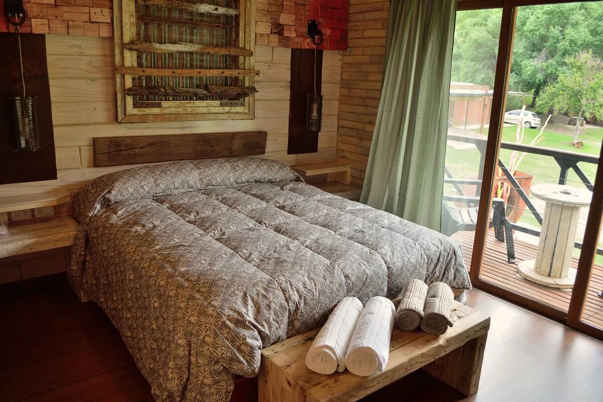 A bedroom with a large bed, wooden headboard, and a view of the outdoors through a large window.