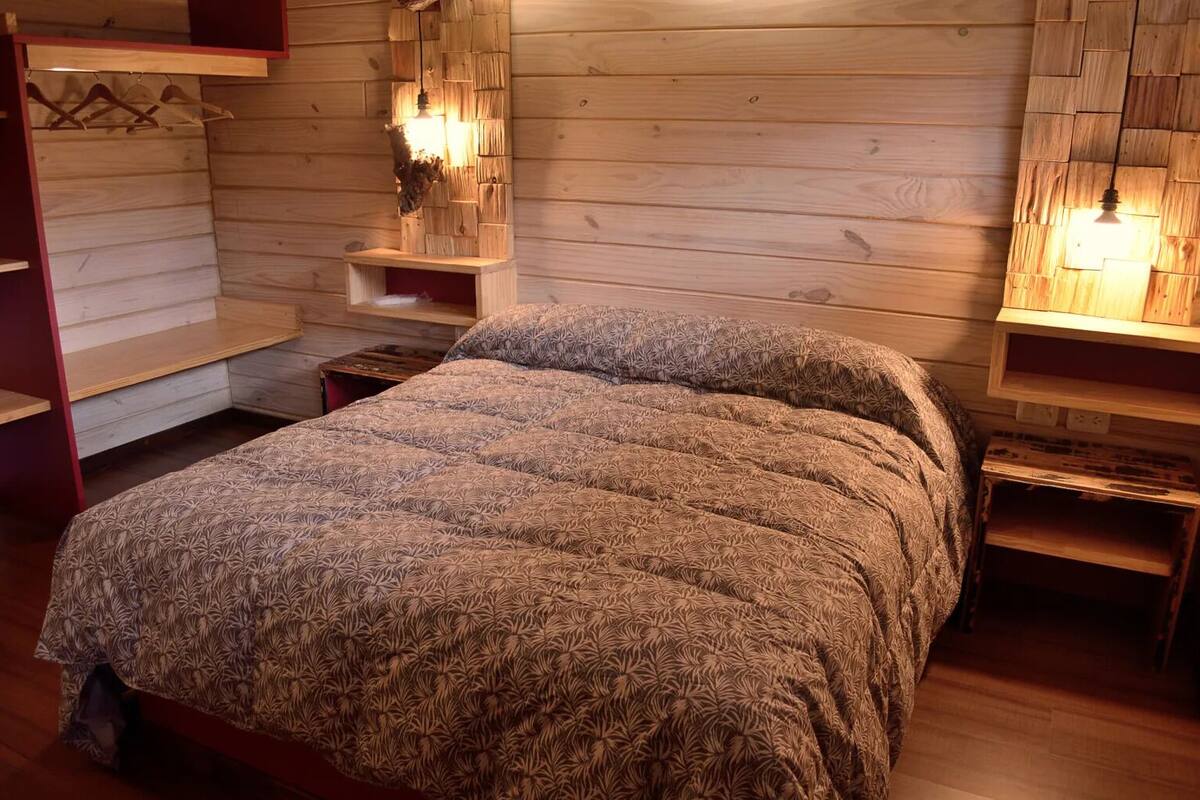 A wooden cabin-style bedroom with a bed, wooden shelves, and wall-mounted lights.