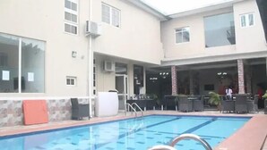 Una piscina con solárium de baldosas, mobiliario exterior y una zona cubierta con bar.