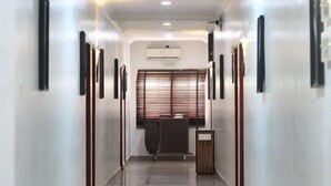 Un pasillo con un equipo de aire acondicionado central, una ventana con persianas y un cubo de basura.