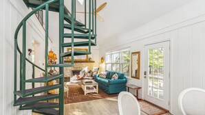 Un salon spacieux avec un escalier en colimaçon, une cheminée, un canapé de couleur turquoise et une grande fenêtre.