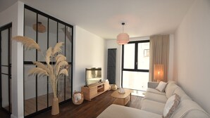 Un salon moderne avec un canapé, une table basse, un téléviseur et une grande fenêtre avec des rideaux.