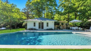 A swimming pool with a small white building and outdoor furniture.