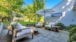 A patio with outdoor furniture, a large umbrella, and a view of a white building.