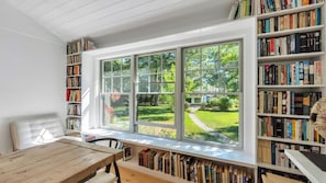 A room with a large window, bookshelves, and a wooden table.