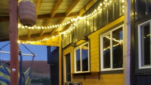 Une terrasse en bois avec un banc et une table, entourée d’une rambarde et illuminée de guirlandes lumineuses.