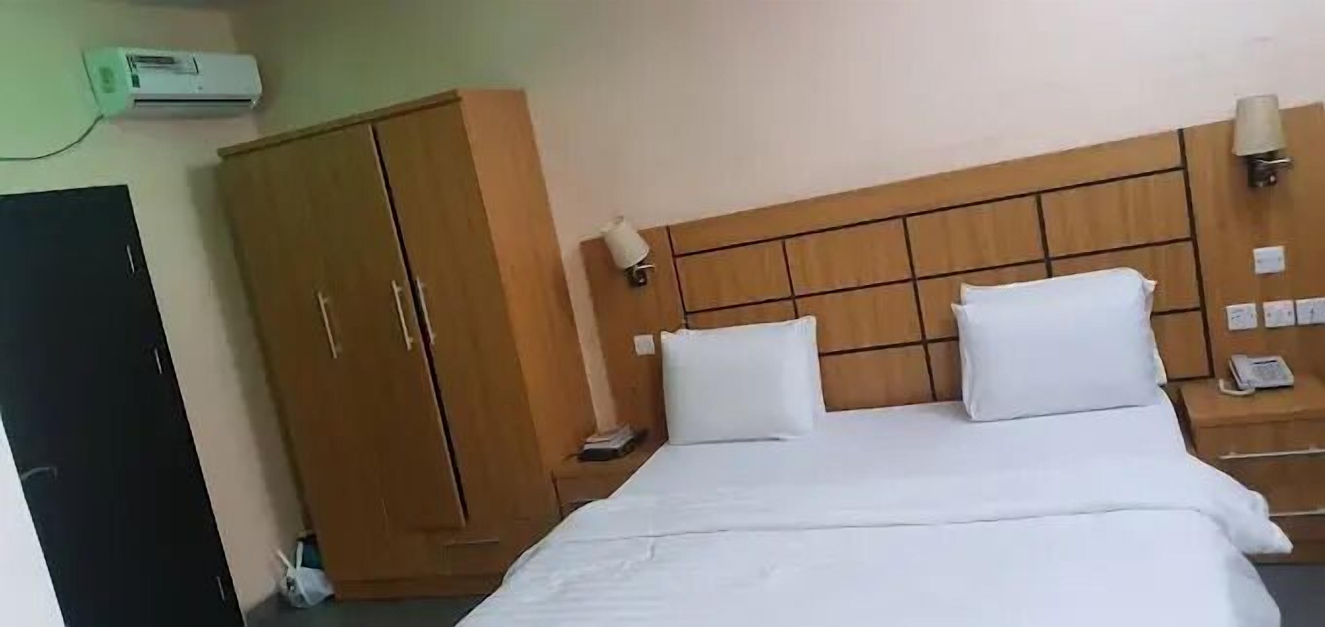 Habitación de hotel con cama, armario, mesita de noche y aire acondicionado de pared.