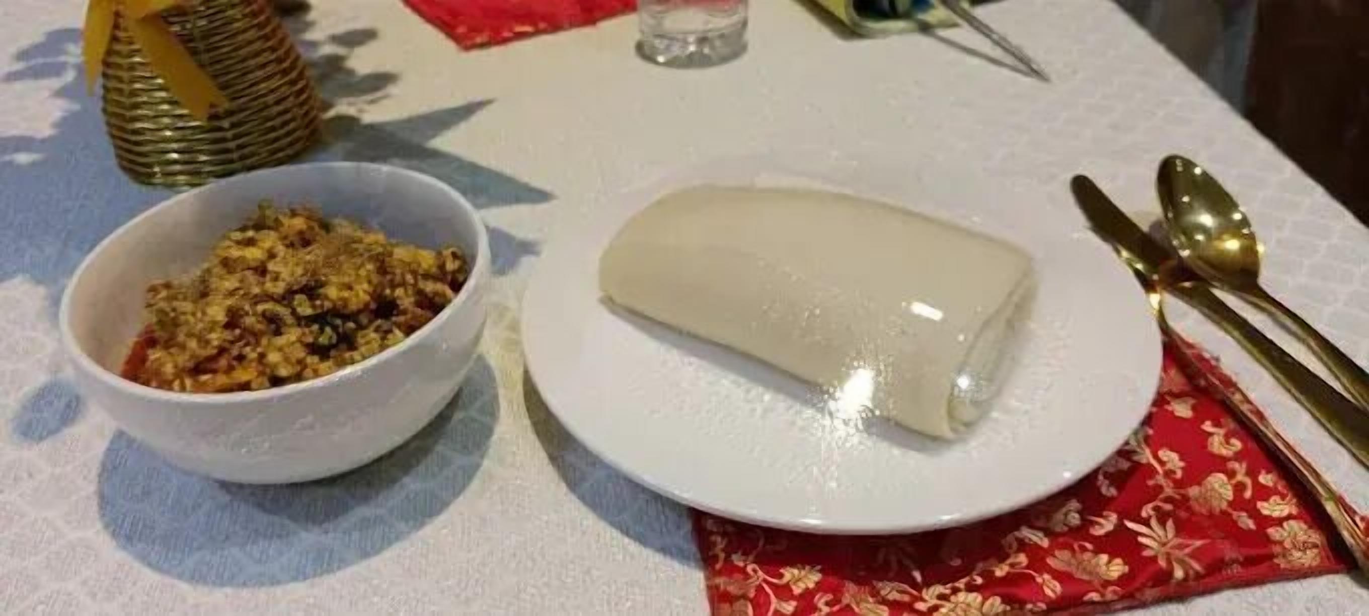 Una mesa con un plato blanco que sostiene un alimento rectangular, un bol con un guiso variado y una cesta decorativa.