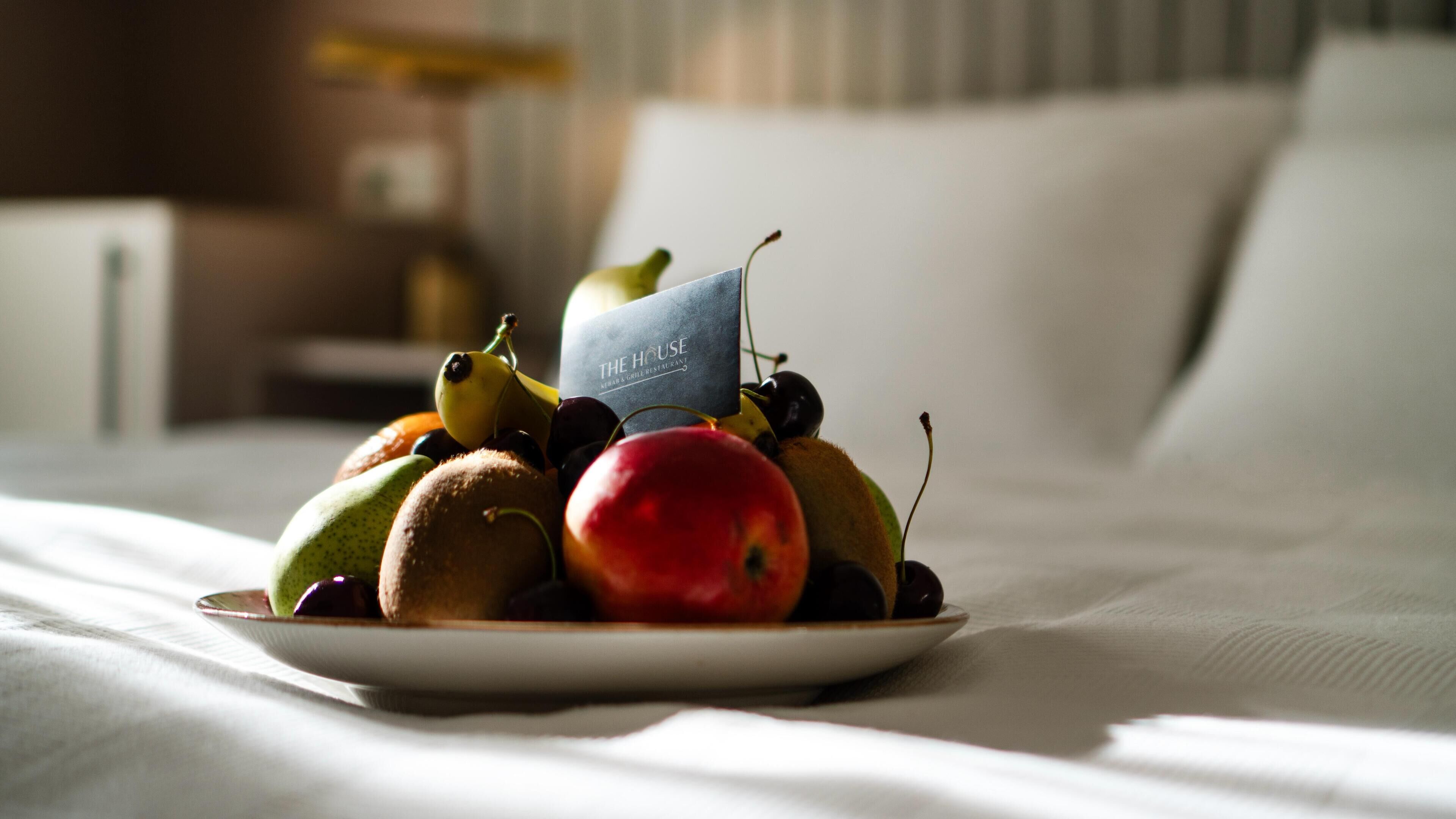 A plate of fruit on a bed with a sign reading "The House".