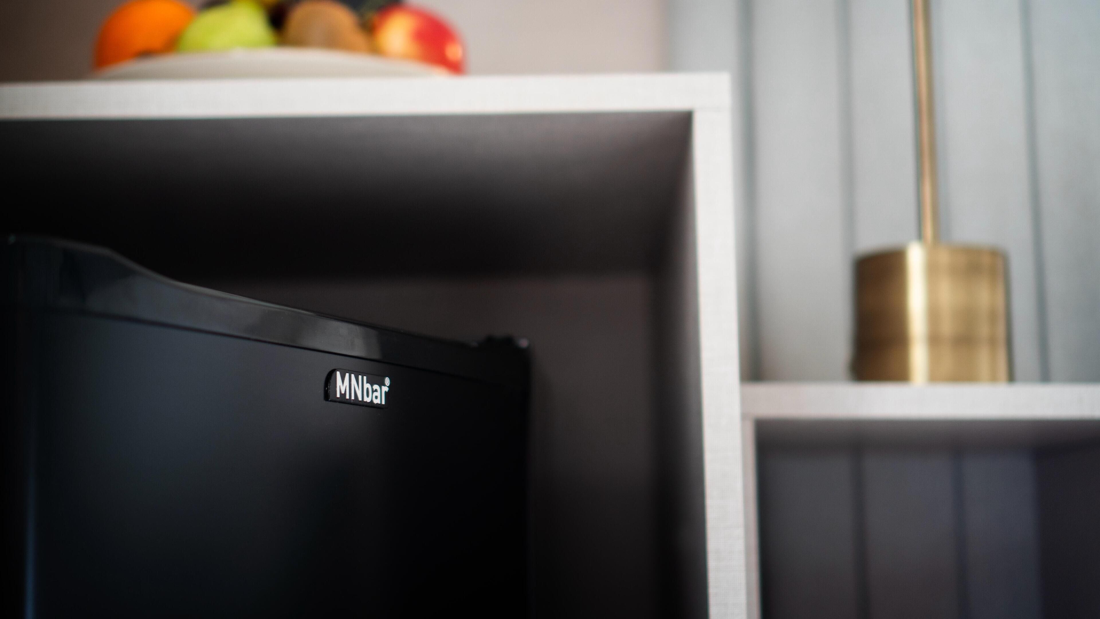 A kitchen with a black appliance labeled "MNbar" and a bowl of fruit on the counter.