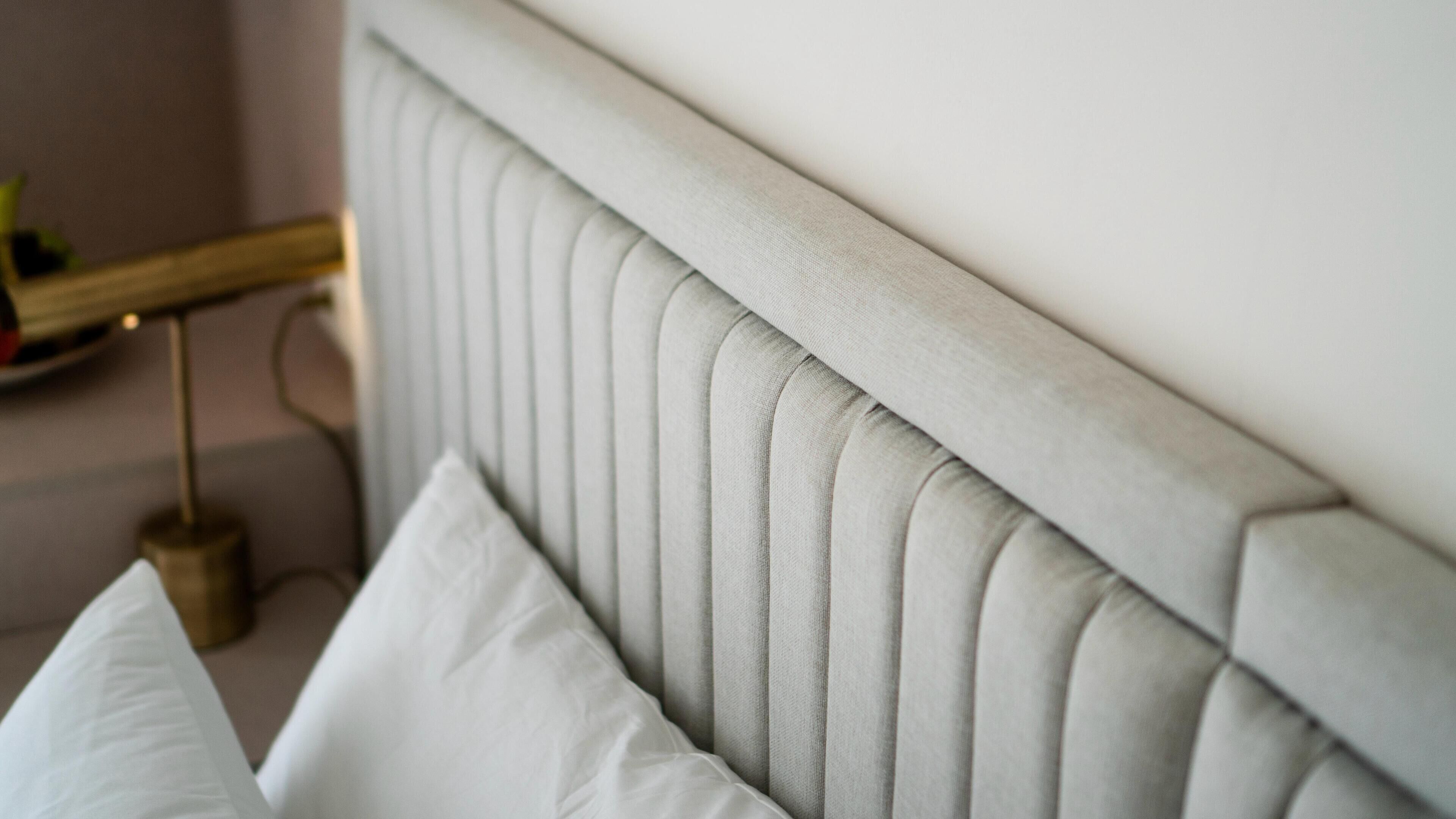 Primer plano de una cama con un cabecero texturizado y almohadas blancas.
