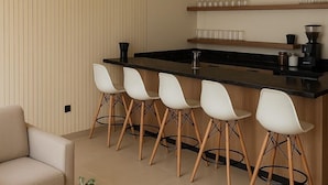 A modern kitchen with a bar area, white bar stools, and a coffee table with a cup and saucer. - Royal Palace Compound (Riyadh)