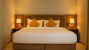 A large bed with a wooden headboard, two bedside lamps, and two decorative pillows. - Royal Palace Compound (Riyadh)