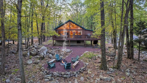 A cabin with a deck, surrounded by trees, and a fire pit with chairs. - The Robin's Nest, a cozy 3-bedroom cabin in Lake Harmony with Firepit, AC, WiFi (Lake Harmony)