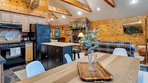A cozy cabin-style kitchen with wooden walls, a stone fireplace, and a dining area with a wooden table and chairs. - The Robin's Nest, a cozy 3-bedroom cabin in Lake Harmony with Firepit, AC, WiFi (Lake Harmony)
