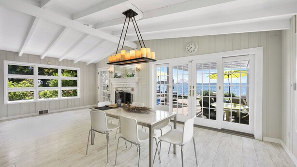 A spacious dining area with a large table, white chairs, and a chandelier.