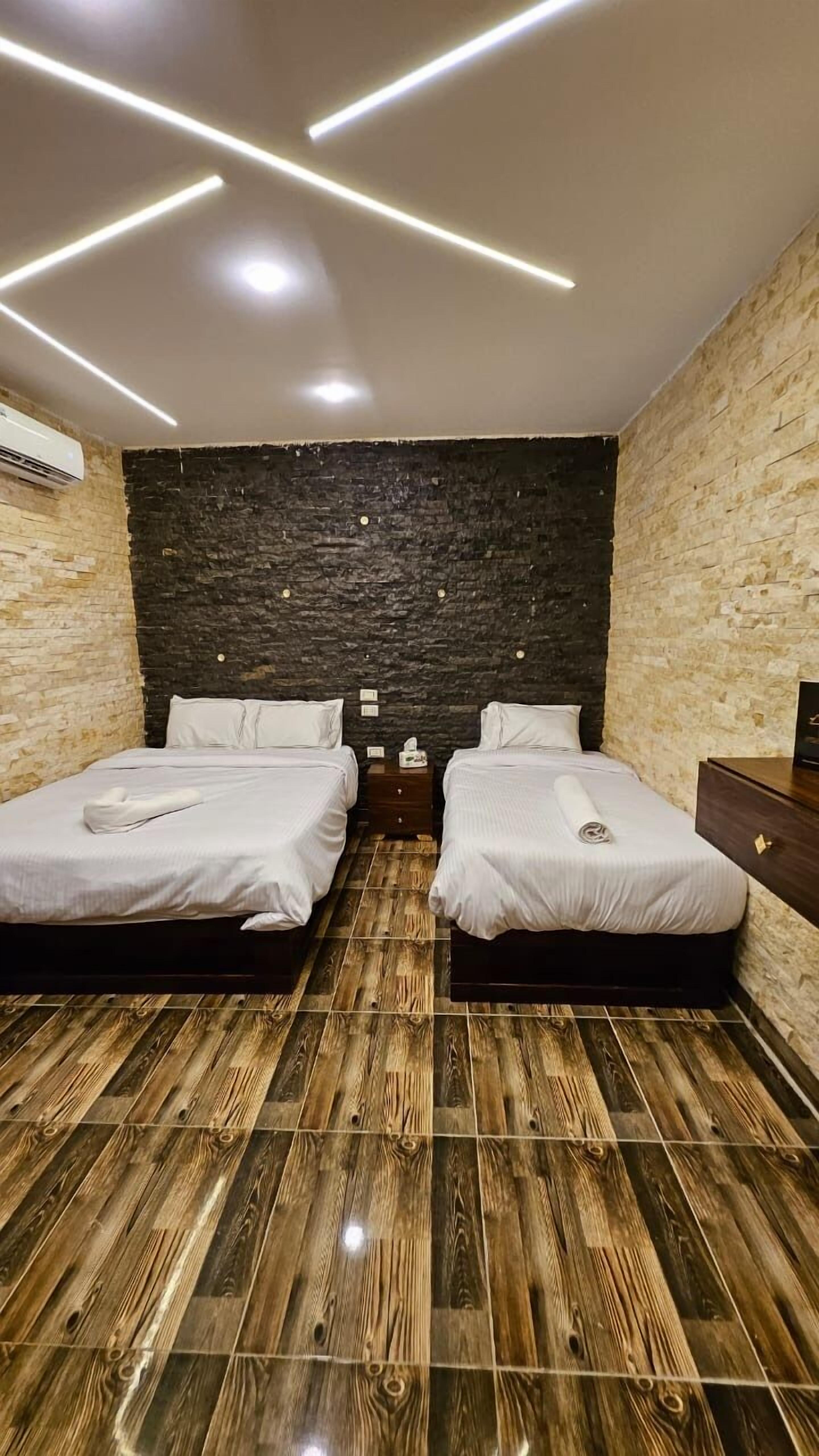 A room with two beds, a dark stone wall, wooden flooring, and modern lighting.