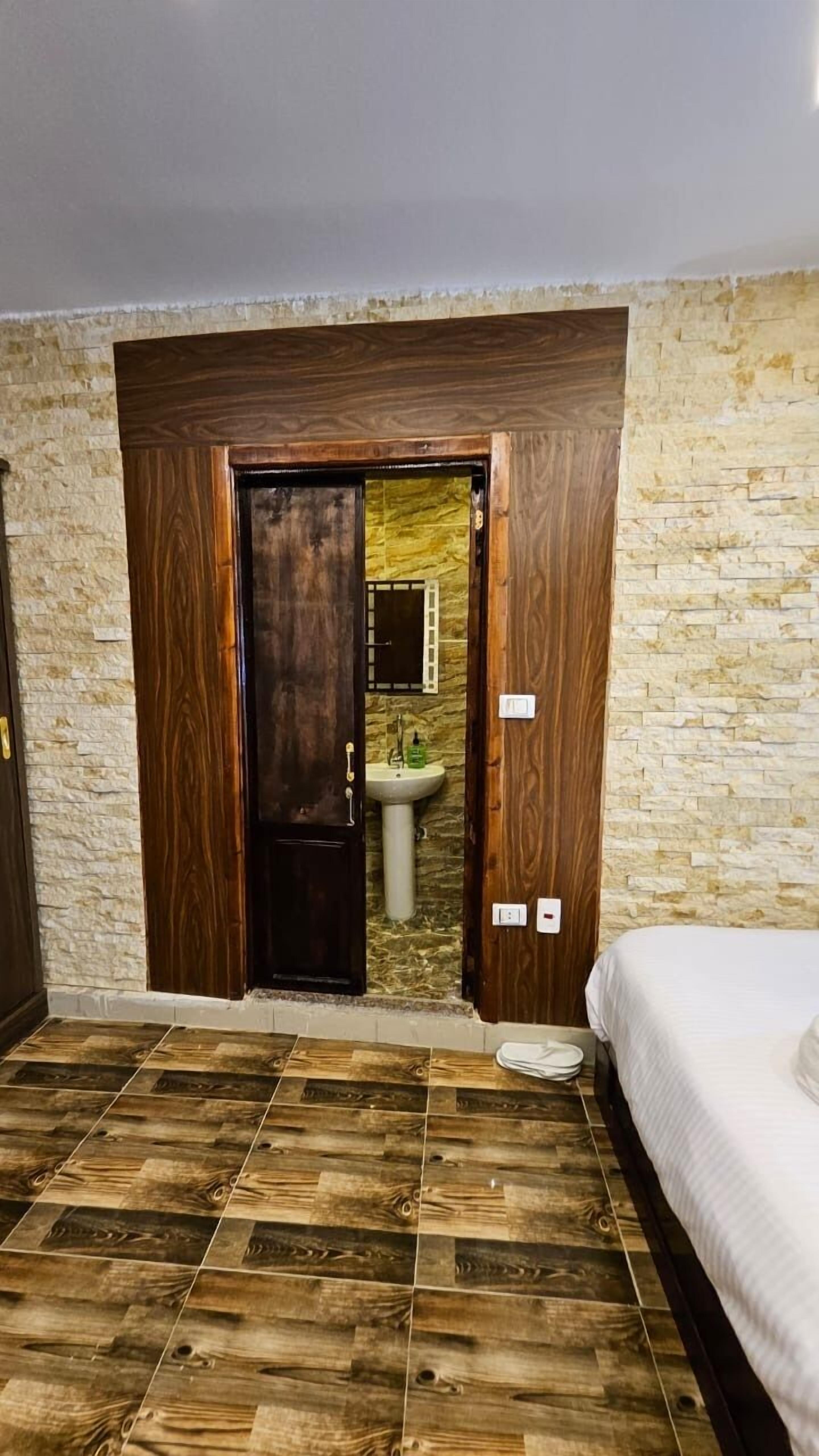 Une chambre avec une porte en bois donnant sur une salle de bain, des murs en pierre et un plancher en bois.