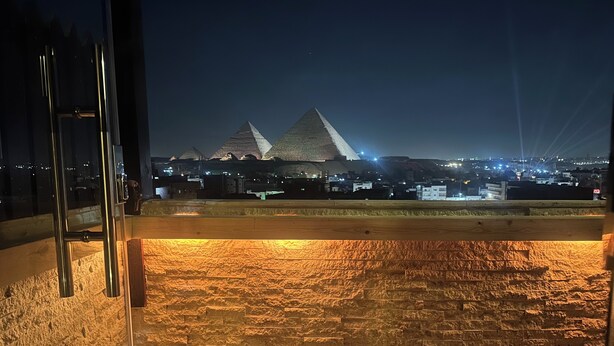 A view of the pyramids at night from a balcony with a stone wall and wooden floor. - Vida Pyramids Inn (Giza)