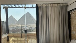 A hotel room with a bed, a window with curtains, and a view of pyramids. - Vida Pyramids Inn (Giza)