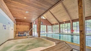 An indoor swimming pool with a wooden interior, a hot tub, and large windows offering views of the outdoors.