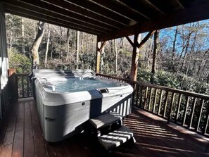 Een hottub op een houten terras met een leuning, omringd door bomen.